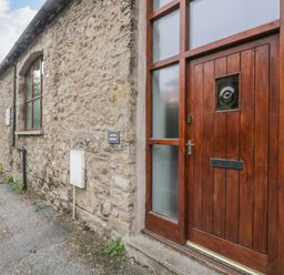 A stone exterior wall with a wooden door and window at Coach House in Arnside