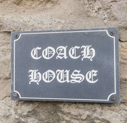 A black rectangular plaque with white decorative font reading Coach House mounted on a stone wall at Coach House in Arnside