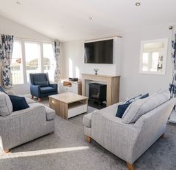 A living room with two grey sofas blue armchair coffee table fireplace and wall mounted television at Dershel Lodge in Southerness