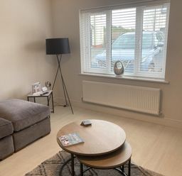 A living room with a gray sofa a black floor lamp two nested round wooden coffee tables and a window showing a parked car at LunaRoxx 6 Meadow Gardens Kilgetty