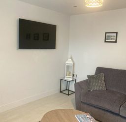 A living room with a mounted TV sofa a side table with candles and two framed pictures on the wall at LunaRoxx 6 Meadow Gardens Kilgetty