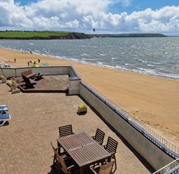 A terrace with a wooden table and chairs and benches overlooking a sandy beach and the sea at High Tide in Duncannon County Wexford
