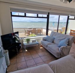 A living room with sofas a television and a dining table overlooking a patio and the sea at High Tide in Duncannon County Wexford