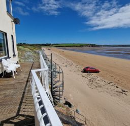 A balcony with two chairs overlooking a sandy beach with a red car and a spiral staircase at Beach House in Duncannon County Wexford