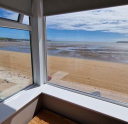 View of a sandy beach and sea from inside a room through corner windows at Beach House in Duncannon County Wexford