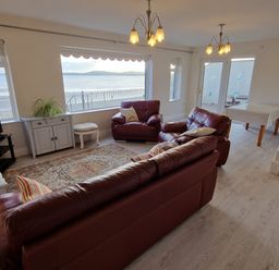 A living room with leather sofas a rug a dining table and large windows overlooking the sea at Beach House in Duncannon County Wexford