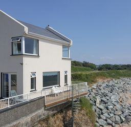 A white two-story house with a balcony overlooking rocky shore and sandy beach at Beach House in Duncannon County Wexford