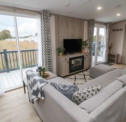 A living room with a gray sofa a television on a cabinet with an electric fireplace and sliding glass doors leading to a balcony at Plot 18 Meadow View in Felton