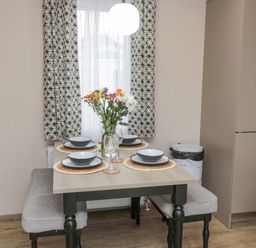 A dining table set with dishes glasses and flowers by a window with patterned curtains at Plot 18 Meadow View in Felton