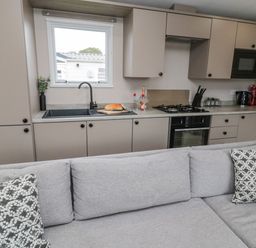 A kitchen with beige cabinets a grey sofa and patterned cushions at Plot 18 Meadow View in Felton
