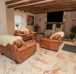 A living room with three brown leather sofas a stone fireplace and wooden ceiling beams at Donni Hall Cottage in Beadnell