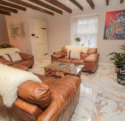 A living room with brown leather sofas a glass coffee table and a colorful animal painting at Donni Hall Cottage in Beadnell
