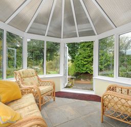 A conservatory with wicker chairs and sofa with cushions and glass windows showing outside at The Wagon House in Lezant near Launceston