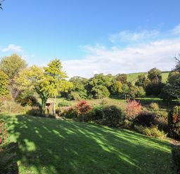 A green lawn with various trees and bushes under a blue sky at The Wagon House in Lezant near Launceston