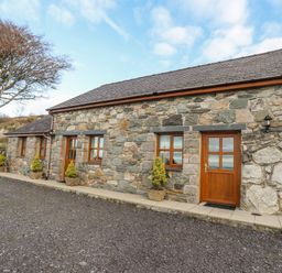 Stone cottage with wooden doors and windows and potted plants outside with a tree nearby at Beech Tree Cottage in Waunfawr