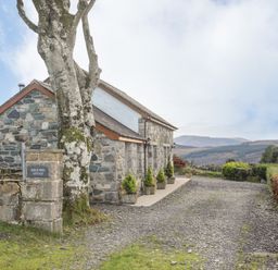 A stone cottage with small potted trees outside and a gravel driveway at Beech Tree Cottage in Waunfawr