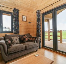 A living room with a brown sofa and pillows next to windows and glass doors leading outside at The Lodge at Crossroads Farm in Middlezoy