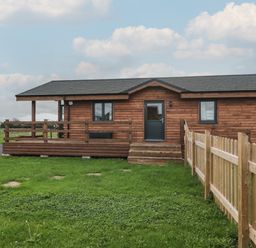 A wooden cabin with a small porch and fenced grassy yard at The Lodge at Crossroads Farm in Middlezoy