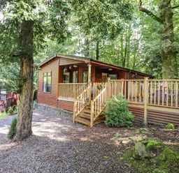 A wooden cabin with a deck and outdoor seating surrounded by trees at Woodland Retreat Skiptory Howe 41A White Cross Bay near Windermere