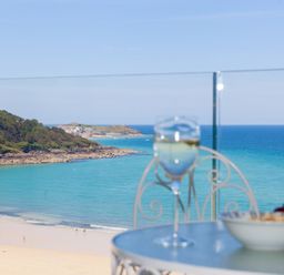 A table with a glass of white wine and a bowl of food overlooking a beach and ocean at Surf and Sand in Carbis Bay