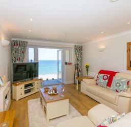A living room with cream sofas and a coffee table overlooking the sea at Surf and Sand in Carbis Bay