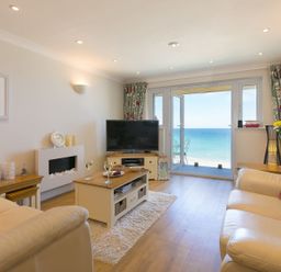 A living room with cream sofas coffee table and television with sea view at Surf and Sand in Carbis Bay