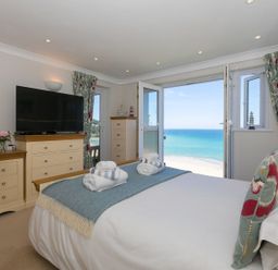 A bedroom with a bed facing open doors to a sea view at Surf and Sand in Carbis Bay