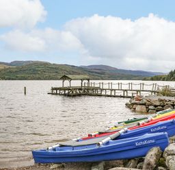 Several colorful kayaks on the shore next to a wooden dock on a lake with hills in the background at Firbush Lodge in Killin