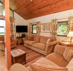A living room with sofas a TV wooden ceiling and windows with curtains at Firbush Lodge in Killin