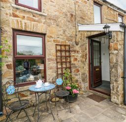 A stone cottage exterior with a small patio table and two chairs near a door at Dunnock Cottage in Broad Haven
