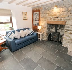 A living room with a blue sofa and striped pillows next to a fireplace with stone walls at Dunnock Cottage in Broad Haven