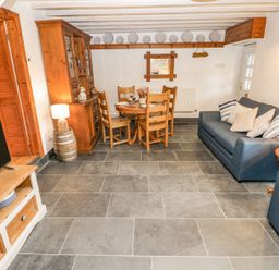 A living room with a wooden dining table and chairs a blue sofa a wooden cabinet and a television at Dunnock Cottage in Broad Haven