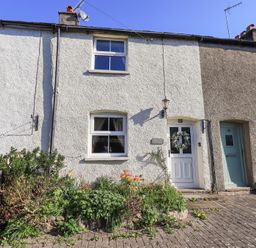 Exterior view of a white terraced house with flower garden and a door with a wreath at Lavender Cottage in Cark In Cartmel