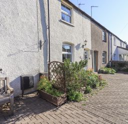 An exterior view of a row of houses with a bench plant box and paved walkway at Lavender Cottage in Cark In Cartmel