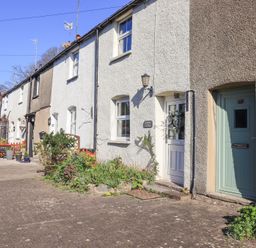 A row of connected cottages with doors and windows along a paved walkway at Lavender Cottage in Cark In Cartmel