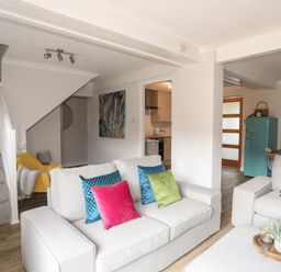A living room with two gray sofas and colorful cushions next to a kitchen and a staircase at 240 Cae Du in Abersoch