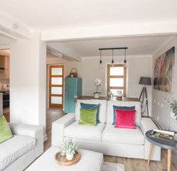 A living room and dining area with beige sofas, colorful cushions, a wooden dining table, a turquoise fridge, and a side table with plants at 240 Cae Du in Abersoch