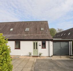 A white house with a green door two potted plants and a grey garage door at 240 Cae Du in Abersoch