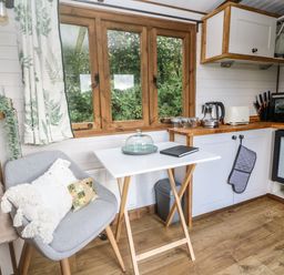 A small kitchen area with a gray chair and white table near a window at Fern in Broad Langdon near Wainhouse Corner