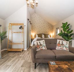 A bedroom with a bed, sofa with duck pillows, wooden shelving, plants and a chandelier at Duck Lodge in Bedale