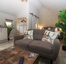 A living area with a gray sofa and duck print cushions a wooden coffee table with a remote control a wooden rack and bed in the background at Duck Lodge in Bedale