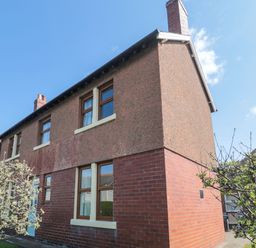 An exterior view of a two-story house with brick and pebble dash walls and windows surrounded by small trees at Bisley House in Amble