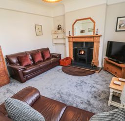A living room with leather sofas a fireplace a wooden chest of drawers a television on a wooden stand and framed pictures at Bisley House in Amble