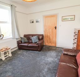 A sitting room with two leather sofas a wooden door a chest of drawers and a small table at Bisley House in Amble