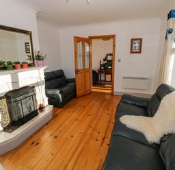 A living room with black leather sofas a white fireplace wooden floor and plants on the mantel at Castle Demesne House in Clifden County Galway