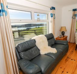 A living room with a dark leather sofa and cream curtains overlooking green hills and water at Castle Demesne House in Clifden County Galway