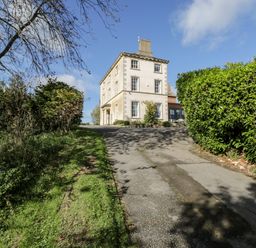 A three story house with windows at the end of a driveway with bushes and trees at Rockstowes House Uley near Dursley