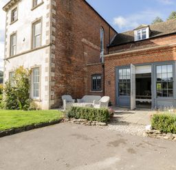 A patio with outdoor seating and open double doors leading into a brick house at Rockstowes House Uley near Dursley