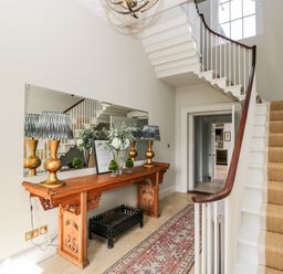 A hallway with a wooden table holding lamps and flowers next to a staircase with carpet at Rockstowes House in Uley near Dursley