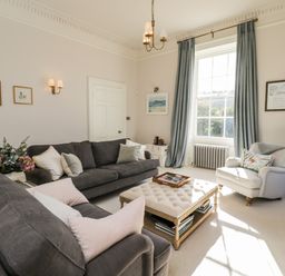 A living room with two dark sofas a white armchair a tufted ottoman and blue curtains at Rockstowes House Uley near Dursley